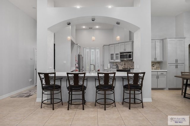 kitchen with a high ceiling, backsplash, gray cabinetry, and hanging light fixtures