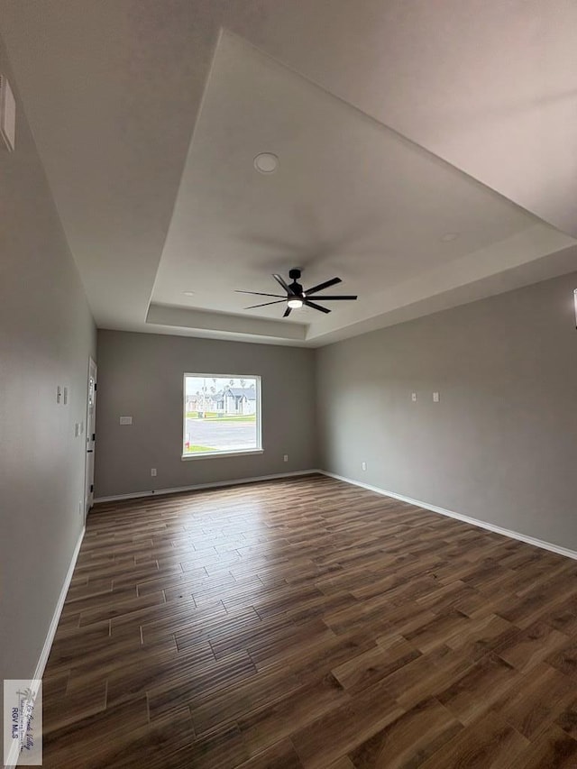 unfurnished room with ceiling fan, baseboards, a raised ceiling, and dark wood-style flooring