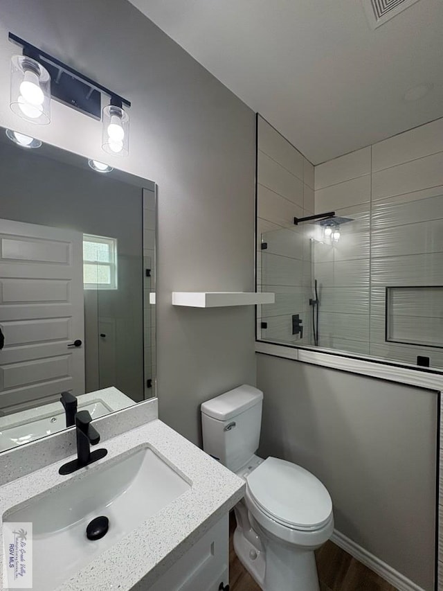 bathroom with visible vents, toilet, vanity, wood finished floors, and tiled shower