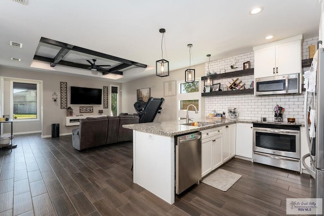 kitchen with backsplash, appliances with stainless steel finishes, white cabinetry, a sink, and a peninsula