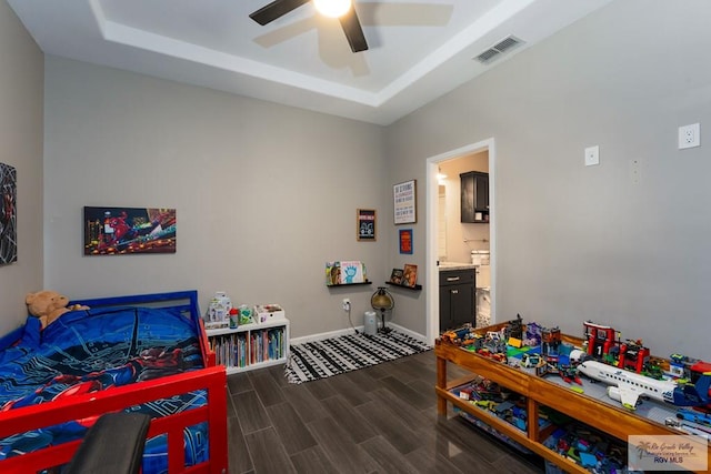 bedroom featuring a tray ceiling, dark wood-style flooring, visible vents, and baseboards