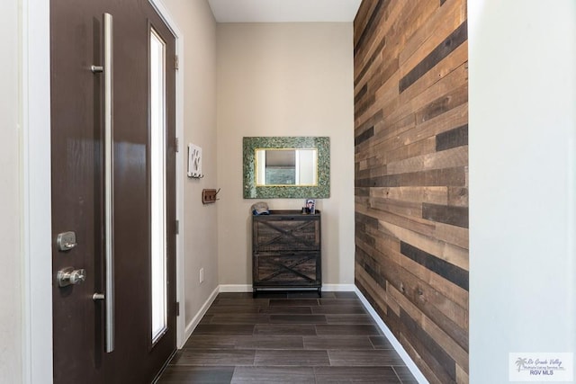 interior space featuring an accent wall, wooden walls, baseboards, and dark wood finished floors