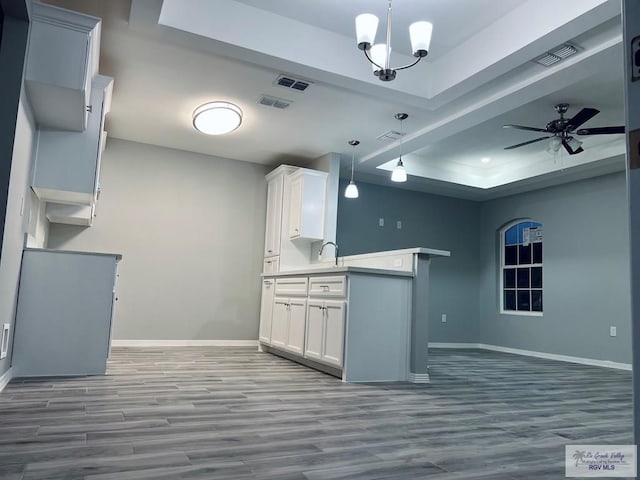 kitchen with hanging light fixtures, hardwood / wood-style floors, a tray ceiling, white cabinetry, and ceiling fan with notable chandelier