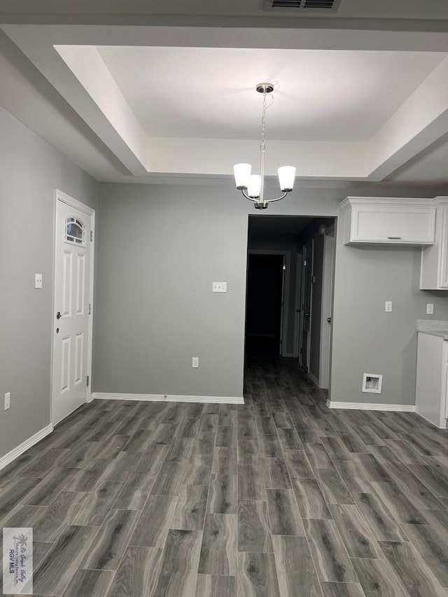 unfurnished dining area with dark wood-type flooring, a raised ceiling, and a chandelier