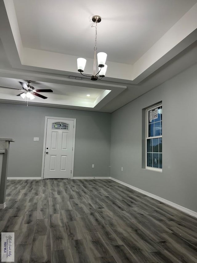 interior space featuring ceiling fan with notable chandelier, a tray ceiling, and dark wood-type flooring