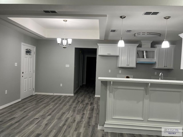 kitchen with dark wood-type flooring, decorative light fixtures, a raised ceiling, an inviting chandelier, and white cabinets