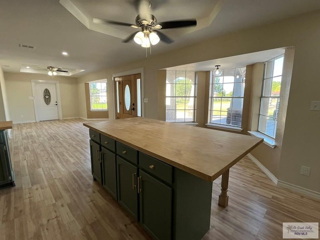 kitchen featuring a center island, butcher block counters, light wood-type flooring, and a tray ceiling