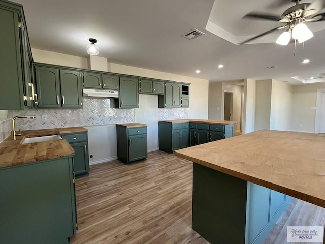 kitchen featuring backsplash, sink, green cabinetry, ceiling fan, and light wood-type flooring