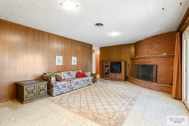 living room featuring wooden walls and a brick fireplace