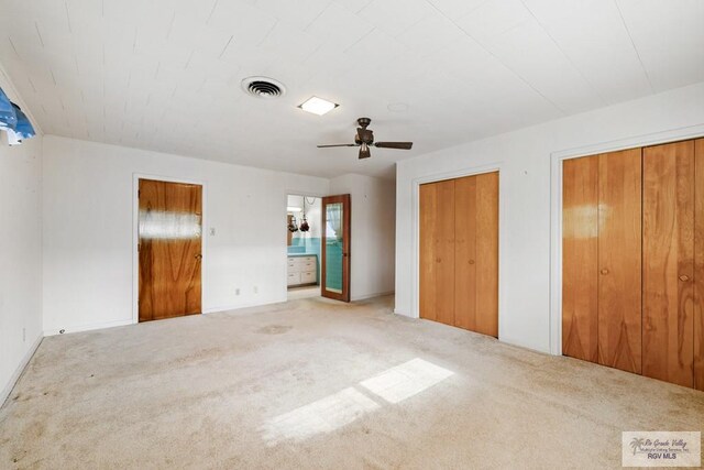 unfurnished bedroom with carpet flooring, ceiling fan, connected bathroom, and two closets