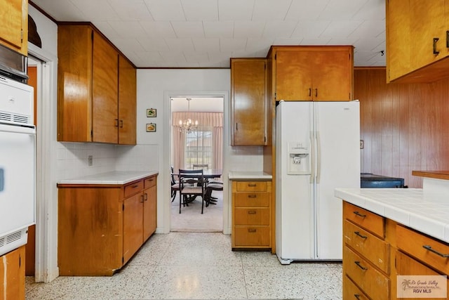 kitchen with tile countertops, white appliances, an inviting chandelier, wooden walls, and tasteful backsplash