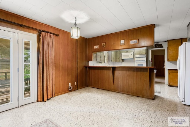 kitchen with pendant lighting, white appliances, wooden walls, kitchen peninsula, and a breakfast bar area