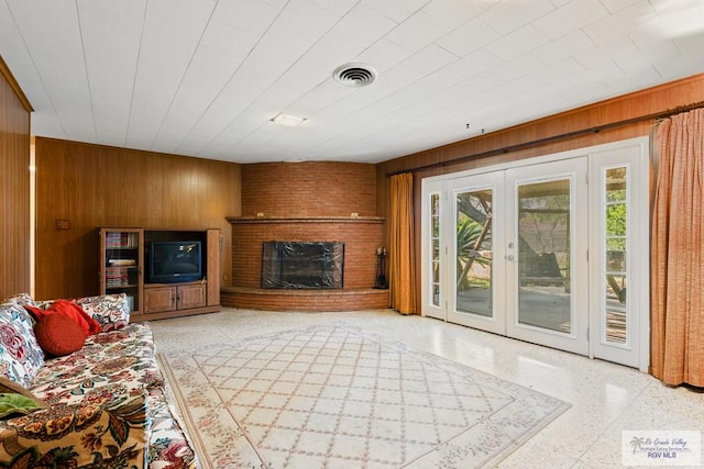 living room with wood walls, french doors, and a brick fireplace