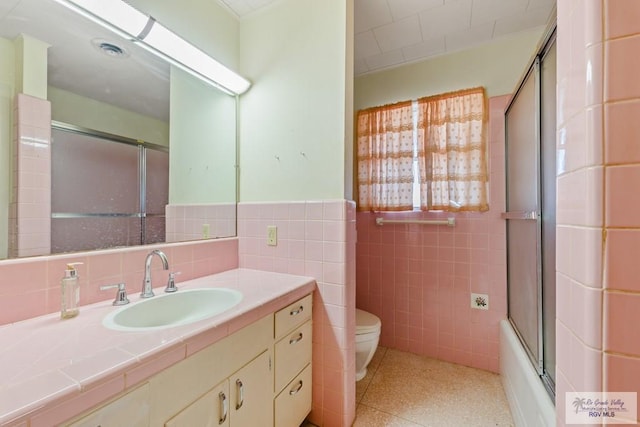 full bathroom featuring vanity, toilet, bath / shower combo with glass door, and tile walls