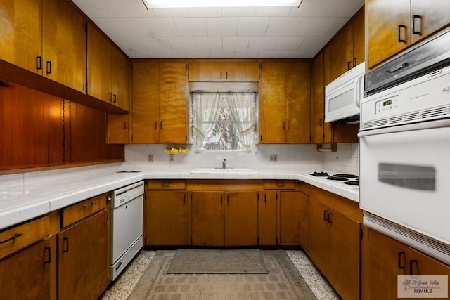 kitchen featuring tasteful backsplash, tile counters, white appliances, and sink