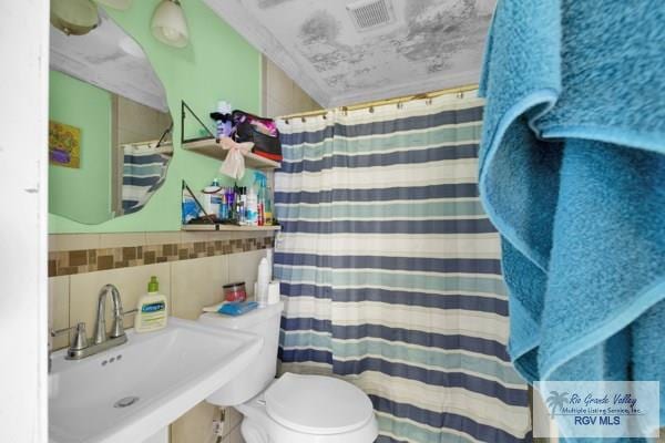 full bathroom featuring visible vents, a sink, tile walls, and toilet