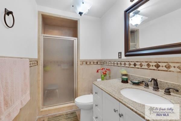 full bathroom featuring a stall shower, toilet, a wainscoted wall, vanity, and tile walls