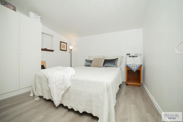 bedroom with vaulted ceiling, light wood-style flooring, and baseboards