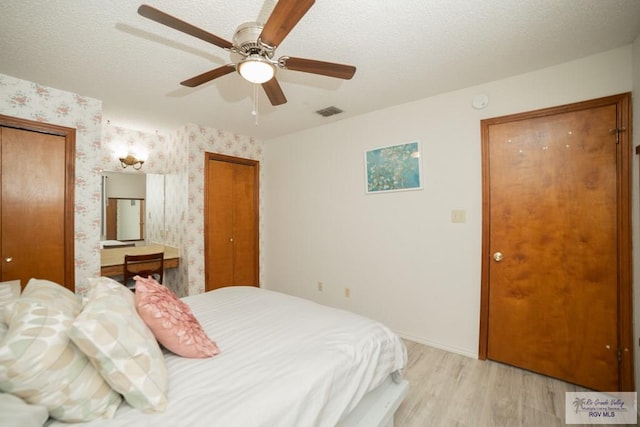 bedroom with a textured ceiling, visible vents, multiple closets, light wood-type flooring, and wallpapered walls