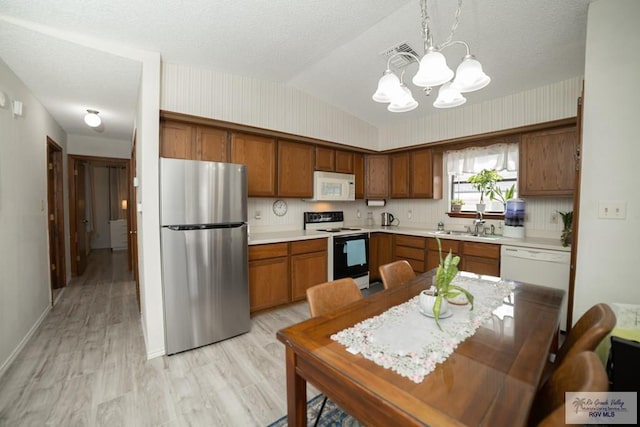 kitchen featuring vaulted ceiling, light countertops, white appliances, and brown cabinetry