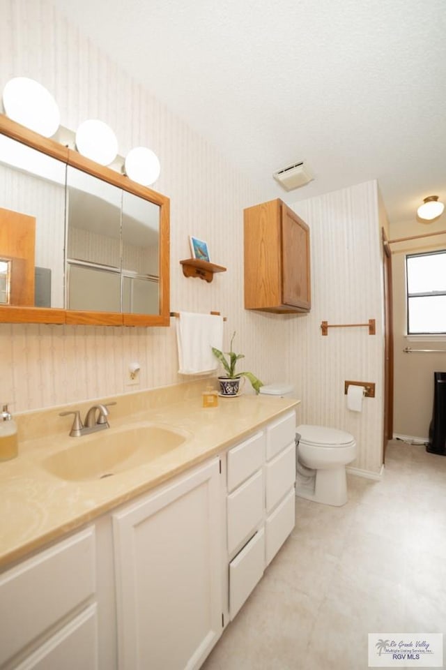 bathroom with toilet, vanity, and wallpapered walls