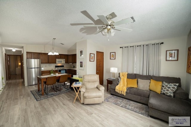 living room featuring vaulted ceiling, a textured ceiling, ceiling fan with notable chandelier, and light wood-style floors