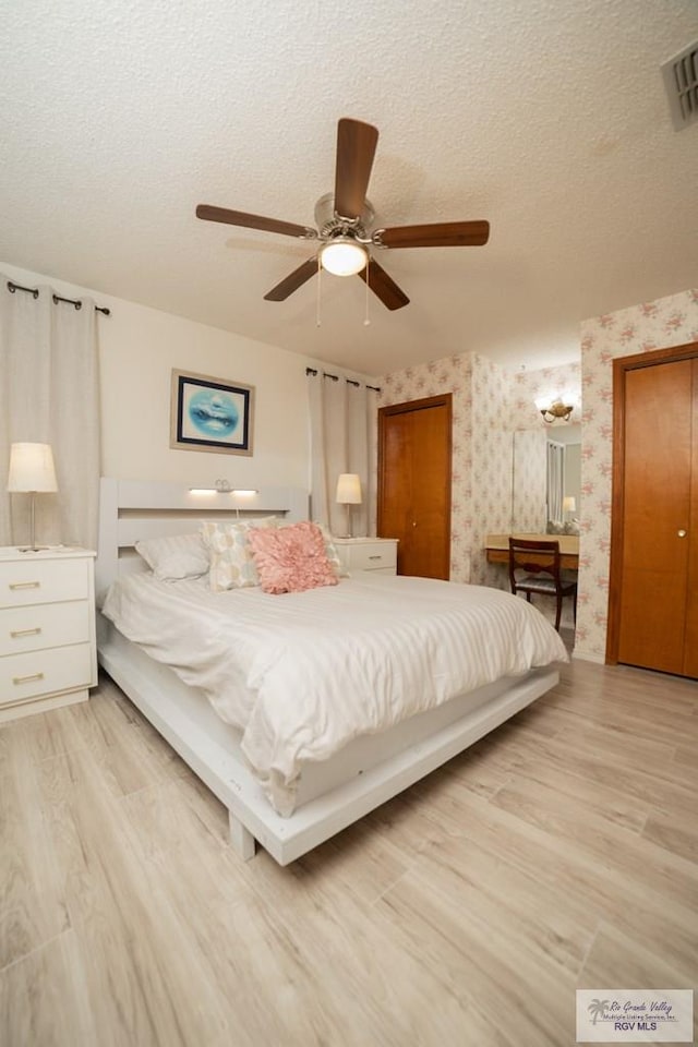 bedroom featuring light wood-style floors, visible vents, a textured ceiling, and wallpapered walls