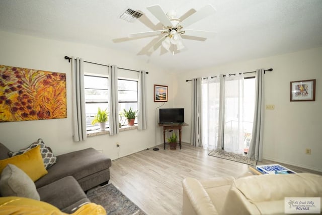 living room with a ceiling fan, visible vents, a wealth of natural light, and wood finished floors