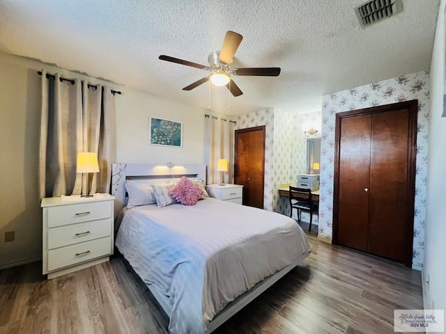 bedroom featuring a textured ceiling, wood finished floors, visible vents, and wallpapered walls