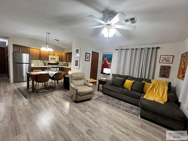 living room featuring lofted ceiling, visible vents, light wood-style floors, a textured ceiling, and ceiling fan with notable chandelier