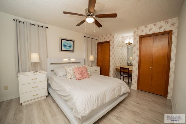 bedroom with wallpapered walls, light wood-style flooring, a textured ceiling, and two closets