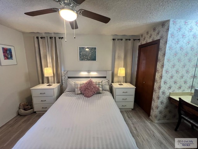 bedroom featuring a textured ceiling, baseboards, wood finished floors, and wallpapered walls