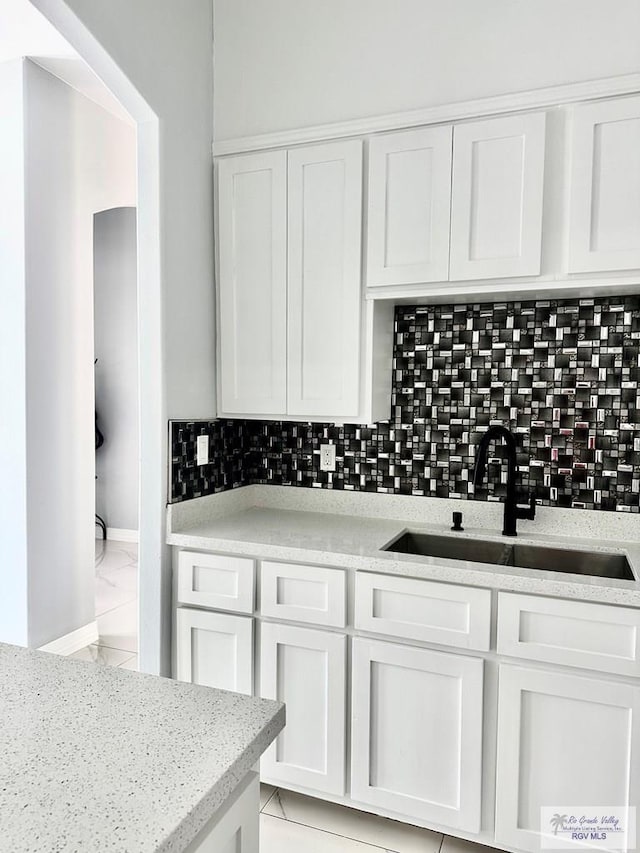 kitchen featuring marble finish floor, decorative backsplash, white cabinetry, a sink, and light stone countertops