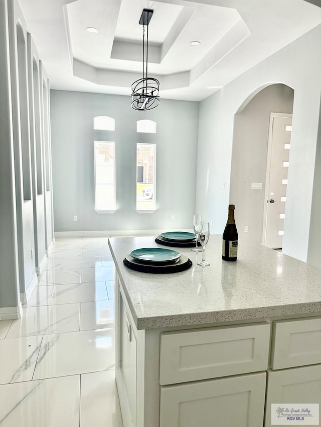 kitchen with light stone counters, baseboards, marble finish floor, a center island, and a tray ceiling