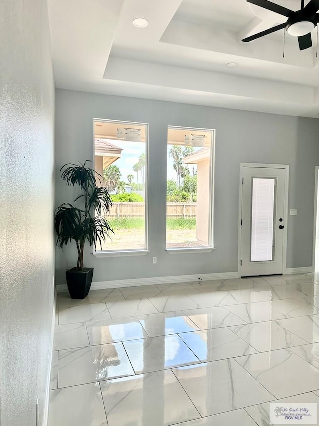 interior space with marble finish floor, baseboards, a tray ceiling, and a ceiling fan