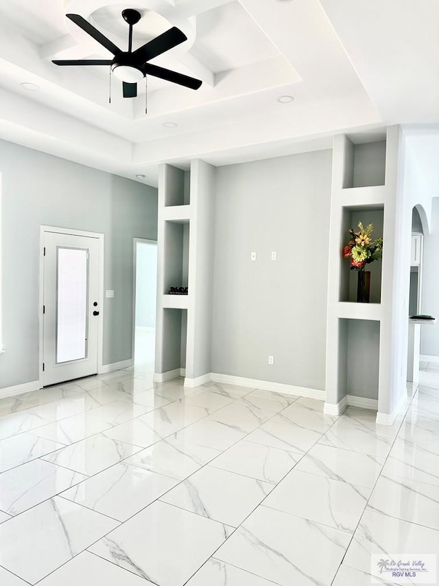 empty room featuring arched walkways, marble finish floor, a raised ceiling, and baseboards