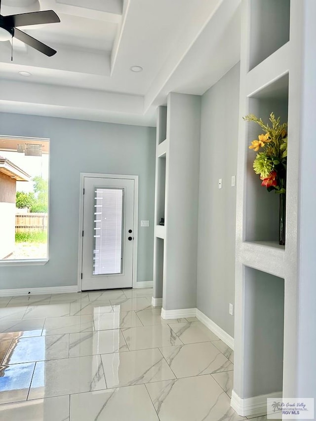 foyer entrance with ceiling fan, marble finish floor, a raised ceiling, and baseboards