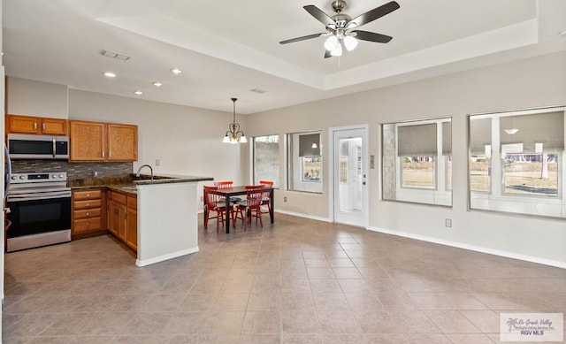 kitchen with brown cabinets, stainless steel appliances, a raised ceiling, a sink, and a peninsula