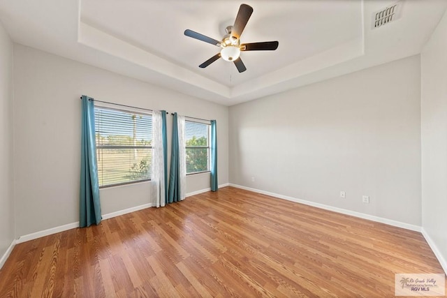 spare room featuring baseboards, a tray ceiling, visible vents, and light wood-style floors