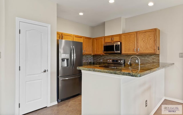 kitchen featuring light tile patterned floors, stainless steel appliances, a peninsula, tasteful backsplash, and dark stone countertops