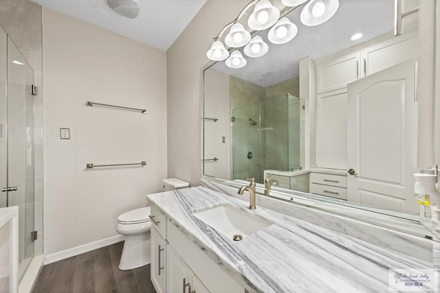 bathroom with toilet, wood finished floors, vanity, baseboards, and a stall shower