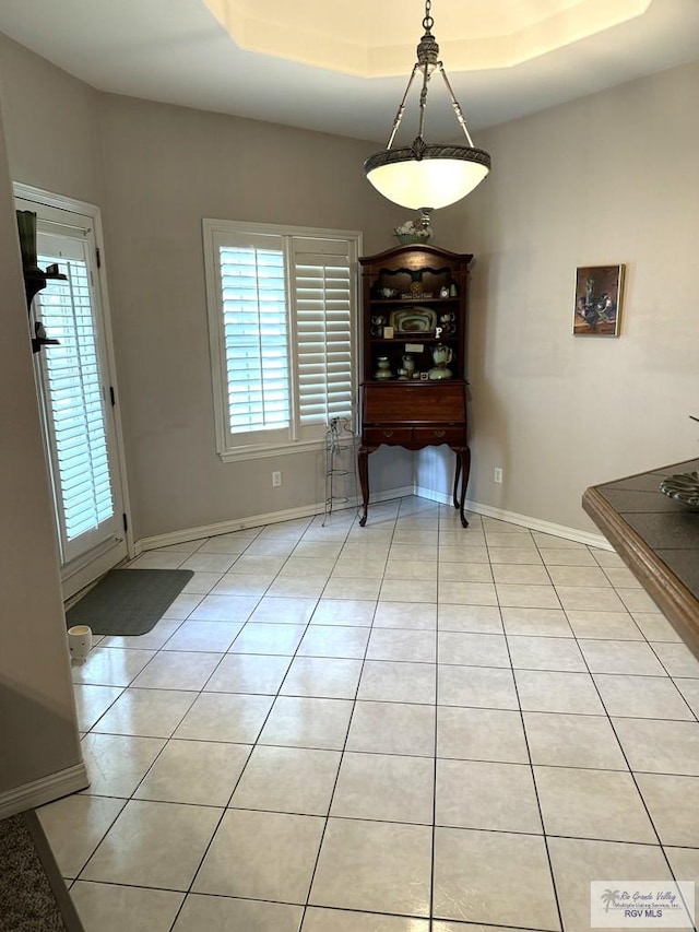 unfurnished dining area featuring light tile patterned floors and a raised ceiling