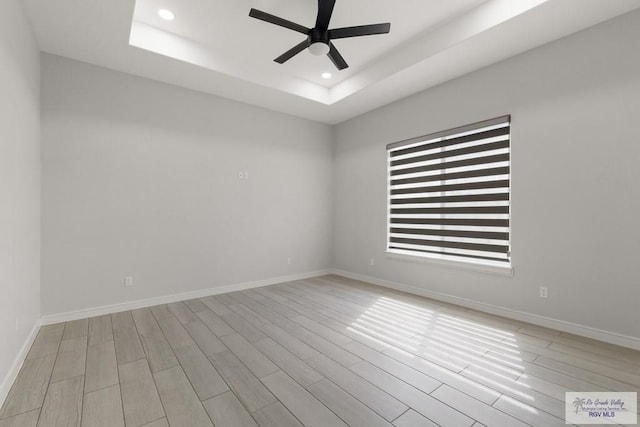 unfurnished room with ceiling fan, a raised ceiling, and light hardwood / wood-style flooring