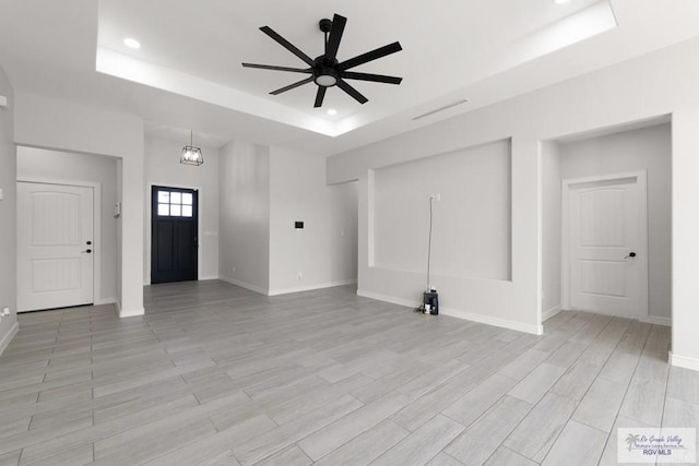 unfurnished living room with ceiling fan with notable chandelier, light wood-type flooring, and a tray ceiling