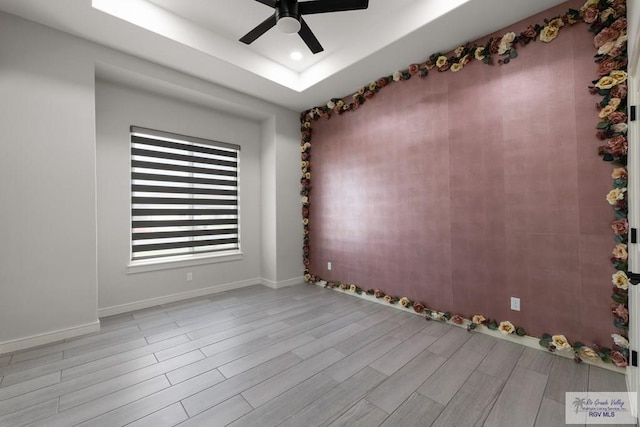 empty room featuring ceiling fan, light hardwood / wood-style floors, and a raised ceiling