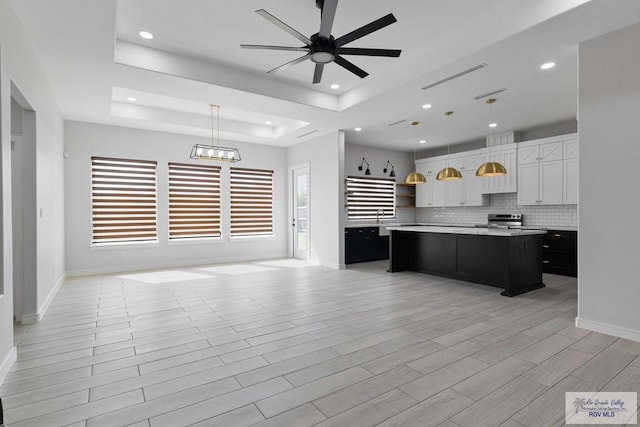 kitchen with decorative light fixtures, a center island, a raised ceiling, and white cabinetry