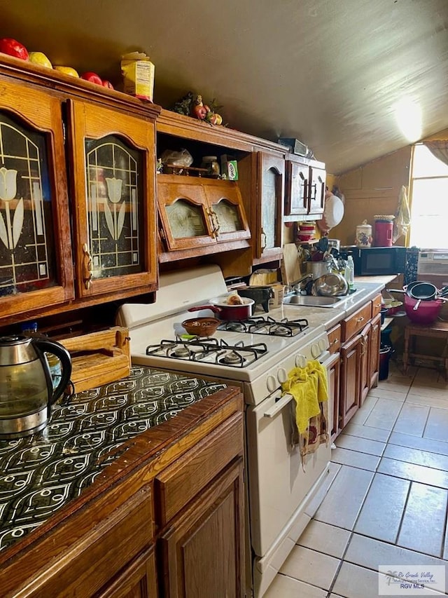 23362 Fm 506, Santa Rosa, TX 78593 - kitchen featuring white range with gas stovetop, vaulted ceiling, light tile patterned flooring, a sink, and brown cabinetry