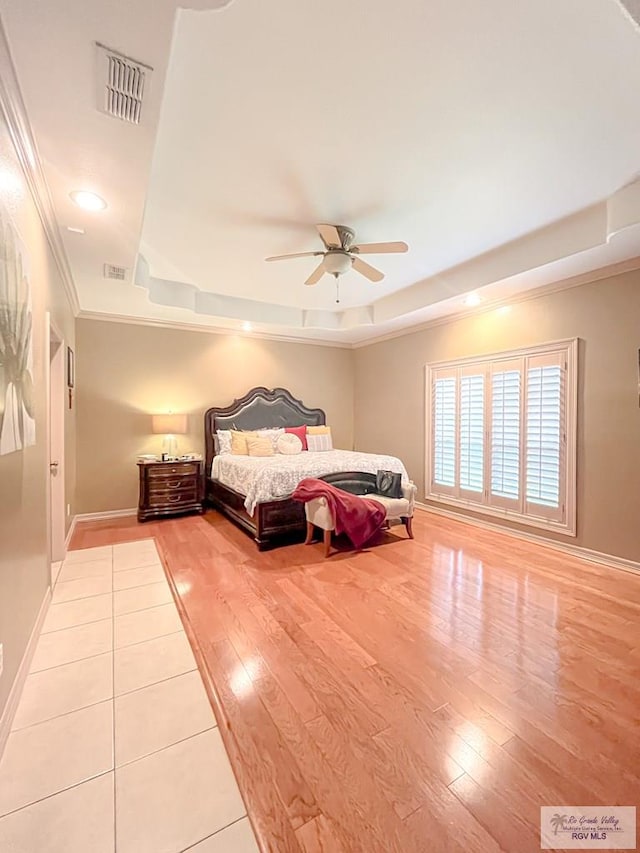 bedroom with ceiling fan, light wood-type flooring, crown molding, and a tray ceiling