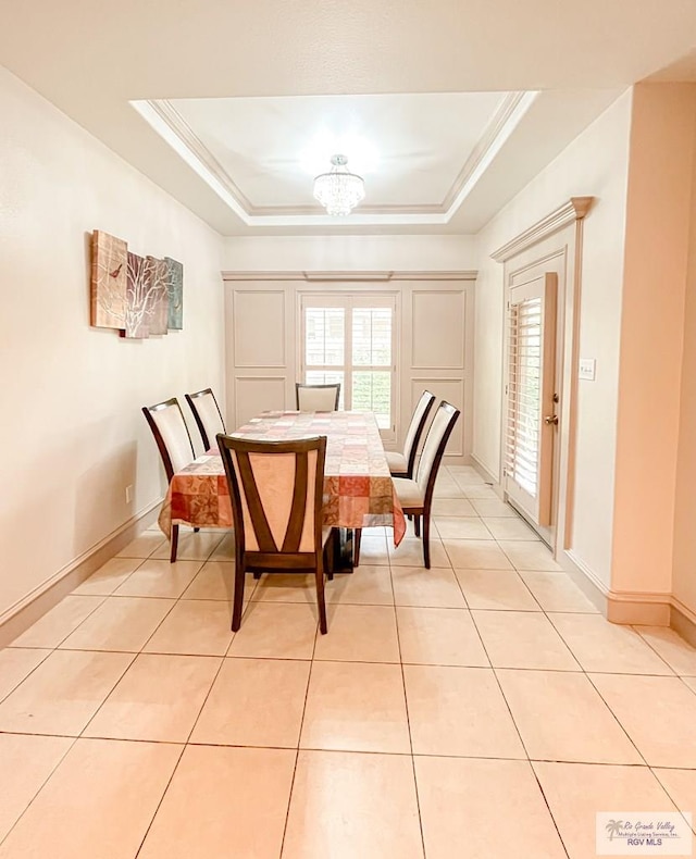 tiled dining area featuring a tray ceiling, a chandelier, and ornamental molding