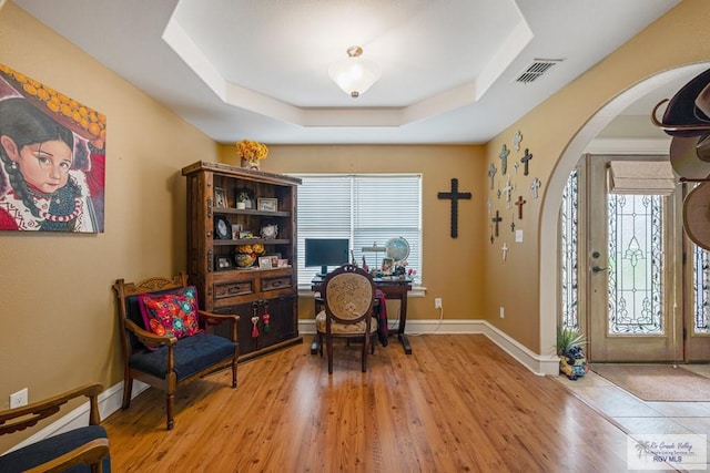 home office with light hardwood / wood-style floors and a raised ceiling